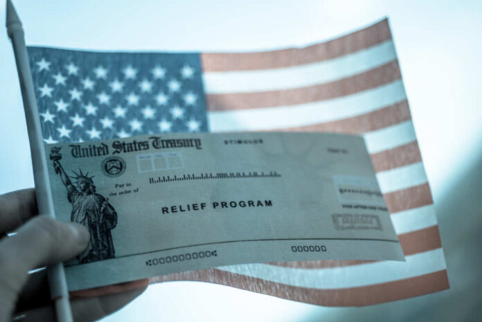 Covid-19,Economic,Stimulus,Check,On,Blurred,Usa,Flag,Background.,Relief