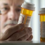 SHOCKING Price Drop Reveals Decades of Overcharging An elderly man holding a prescription bottle while examining it closely