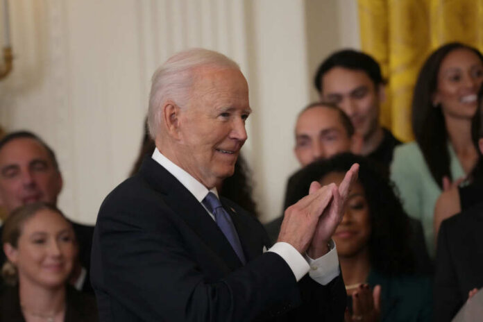 A smiling man in a suit clapping during a formal event with a crowd in the background