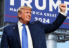 A man in a suit raises his fist in front of a large campaign sign