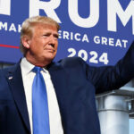 A man in a suit raises his fist in front of a large campaign sign