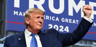 A man in a suit raises his fist in front of a large campaign sign