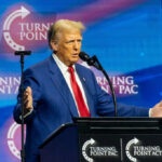 Trump Agenda Roars Free–Judges Sidelined A man in a blue suit speaking at a podium with a microphone