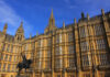 The Palace of Westminster with a statue in the foreground under a blue sky