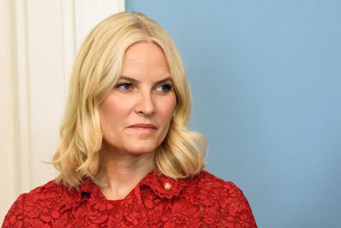 A woman with blonde hair wearing a red lace dress, looking serious