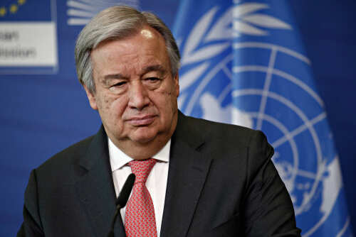 A political leader speaking at a press conference with a serious expression