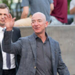 A man waving at a crowd while accompanied by a security guard