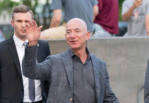 A man waving at a crowd while accompanied by a security guard