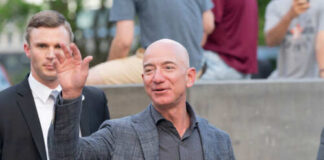 A man waving at a crowd while accompanied by a security guard