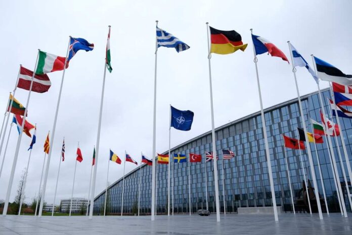 Flags of various countries in front of a modern building under a cloudy sky