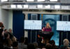 A woman speaking at a podium during a White House press briefing with journalists in attendance