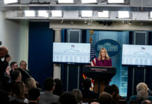A woman speaking at a podium during a White House press briefing with journalists in attendance