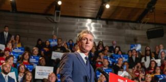 A speaker addressing a crowd at a political rally with signs in the background