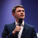 A man in a suit speaking into a microphone at a conference