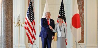 Two political leaders shaking hands in front of flags