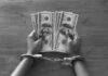 Hands in handcuffs holding stacks of cash