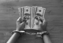 Hands in handcuffs holding stacks of cash