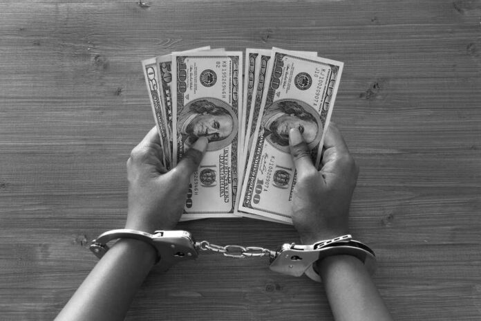 Hands in handcuffs holding stacks of cash