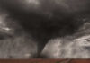 A tornado forming in a dark, stormy sky over a field