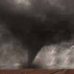 A tornado forming in a dark, stormy sky over a field
