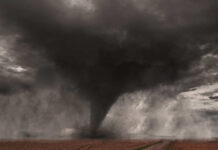 A tornado forming in a dark, stormy sky over a field