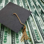 A graduation cap placed on a stack of hundred dollar bills