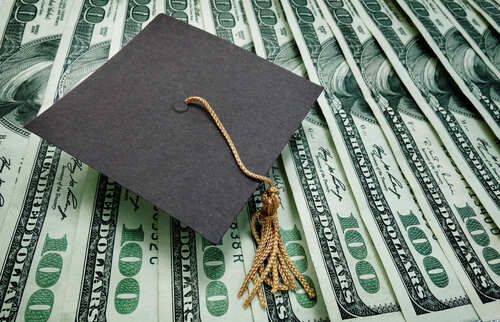 A graduation cap placed on a stack of hundred dollar bills