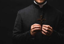 Clergy member holding a wooden cross against a dark background