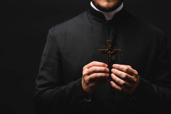 Clergy member holding a wooden cross against a dark background