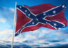 Confederate flag waving against a blue sky with clouds