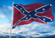 Confederate flag waving against a blue sky with clouds
