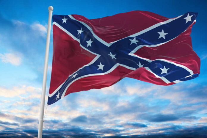 Confederate flag waving against a blue sky with clouds