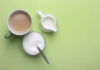 A cup of coffee, a bowl of sugar, and a creamer on a green background