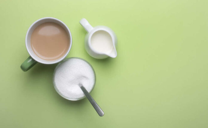 A cup of coffee, a bowl of sugar, and a creamer on a green background
