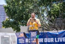 Speaker at a rally holding a microphone with a banner in the background