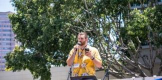 Speaker at a rally holding a microphone with a banner in the background