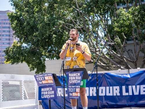 Speaker at a rally holding a microphone with a banner in the background