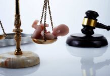 Scales of justice with a baby figurine and a gavel in the background