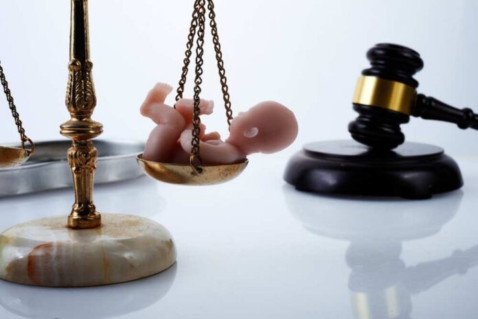 Scales of justice with a baby figurine and a gavel in the background