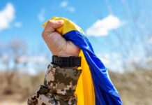 A soldier holding a blue and yellow flag against a bright sky