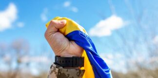A soldier holding a blue and yellow flag against a bright sky