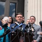 A group of individuals at a press conference with a speaker at a podium
