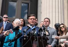 A group of individuals at a press conference with a speaker at a podium