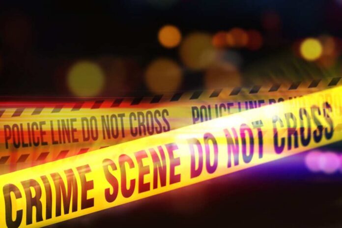 shutterstock_2521773821.jpg Yellow police tape marking a crime scene with blurred lights in the background