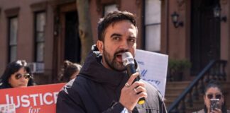 Man speaking into a microphone at a public rally for senior justice