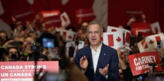 Mark Carney speaking at a political rally with supporters holding signs