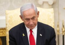 A government official with a serious expression seated in a formal setting