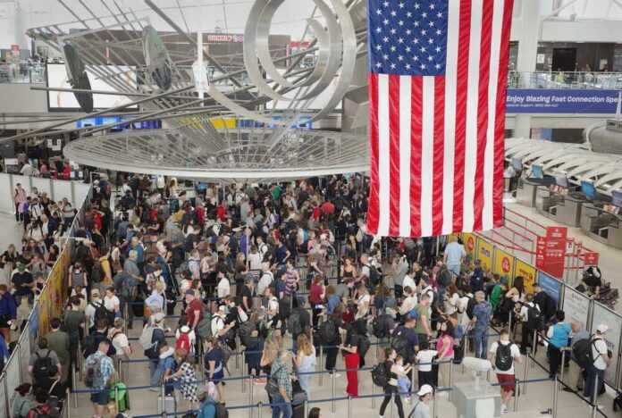 Crowd of travelers waiting in line at an airport security checkpoint under an American flag