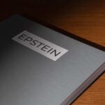 A metallic folder labeled 'EPSTEIN' resting on a wooden surface