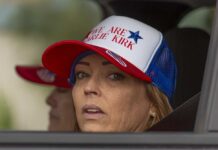 A woman wearing a cap with a political message, looking out from a vehicle